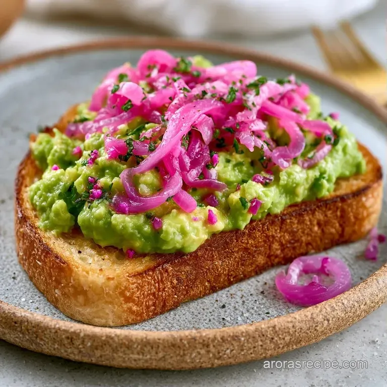 Two slices of golden toast on a white ceramic plate, topped with mashed green avocado and bright pink onion rings