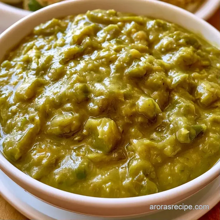 Vibrant green stew in a white bowl topped with melted Monterey Jack cheese and a slice of lime on a linen cloth.